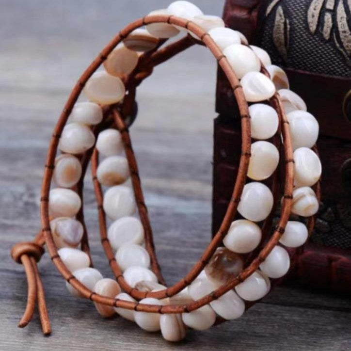 White shell bead bracelet with brown braided straps, layered wrap-style design.