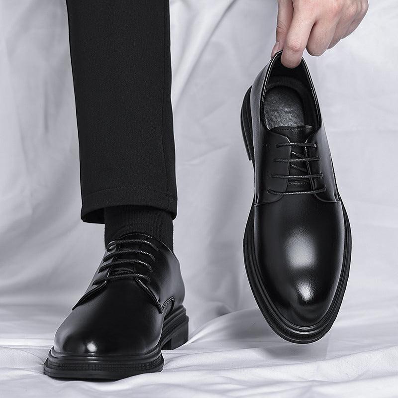Black leather lace-up dress shoes with rounded toe and thick sole, held upright.