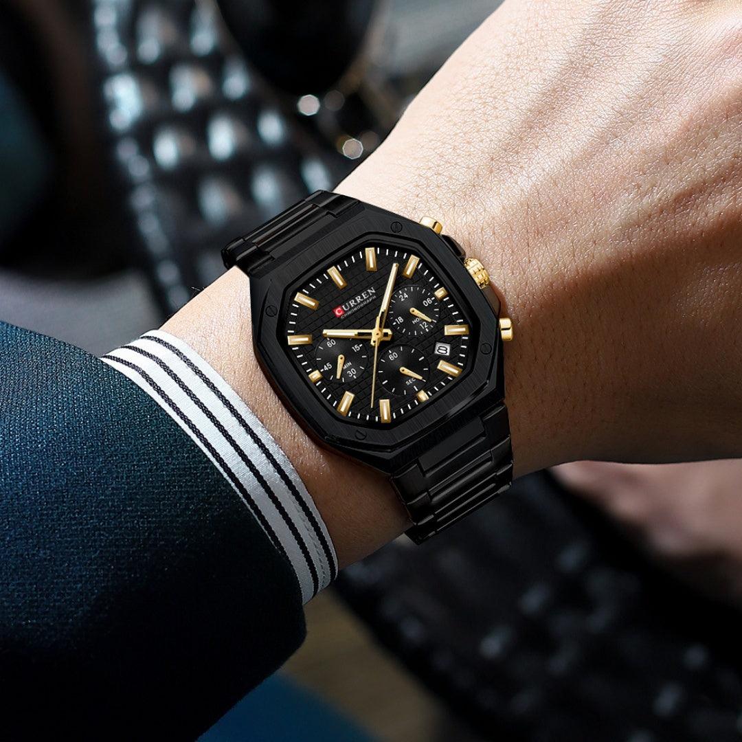 Black six-pin calendar business steel watch with black dial and gold-tone markers, on wrist