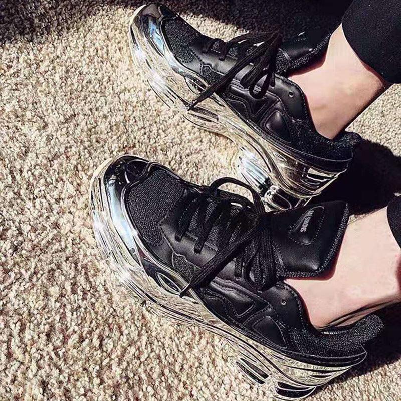 Black lace-up chunky sneakers with metallic chrome platform soles on outdoor gravel