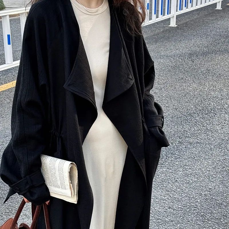 Black trench coat with wide lapels and long sleeves, open draped front