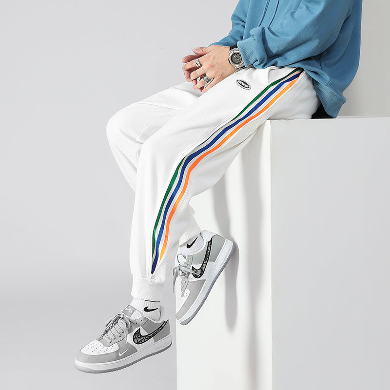 Men's white tapered track pants with multicolor side stripe and logo patch