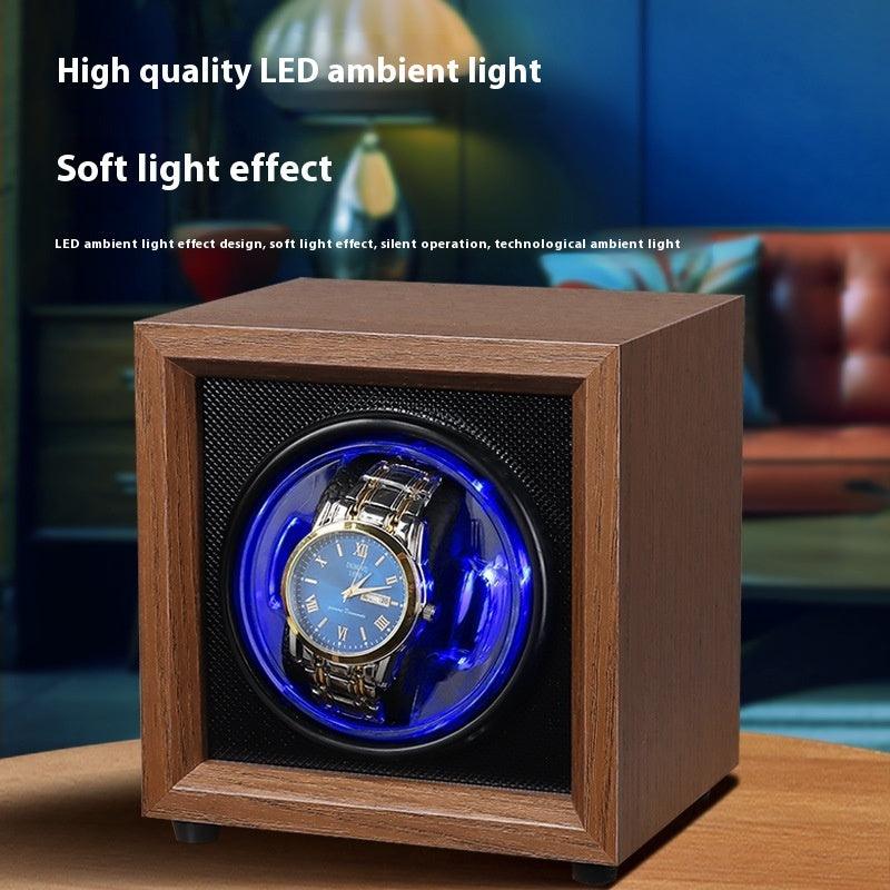 Wood watch winder with blue LED glow around the circular window and an automatic wristwatch.