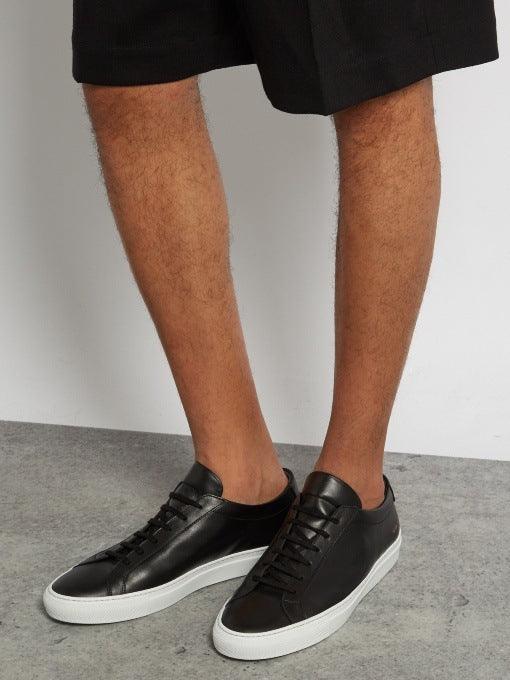 Black leather lace-up sneakers with white sole, worn with black shorts and socks.