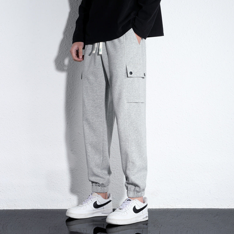 Light gray cotton jogger trousers with drawstring waist, elastic cuffs, and side cargo flap pocket