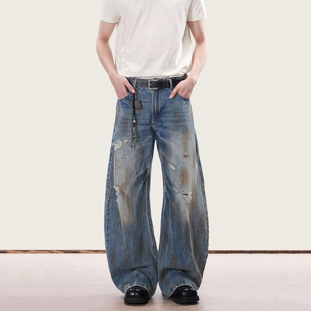 Blue stain-dyed jeans with sparse rips and distressed patches, wide-leg fit, black belt