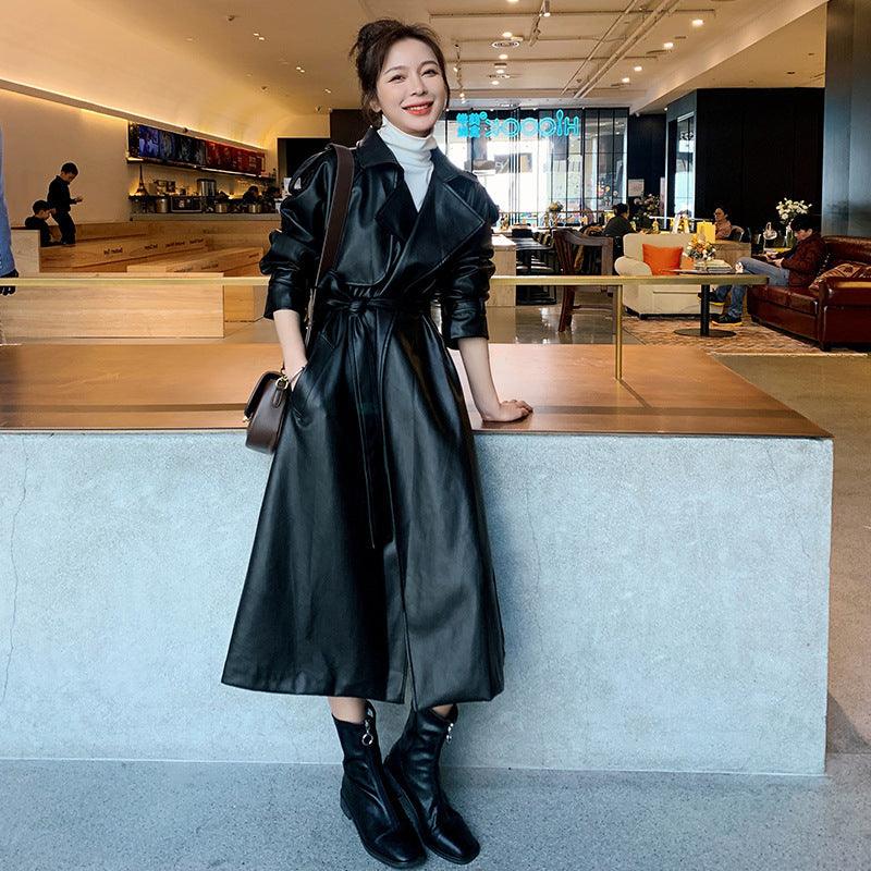 Black leather trench coat with belted waist, notched lapels, and long sleeves.