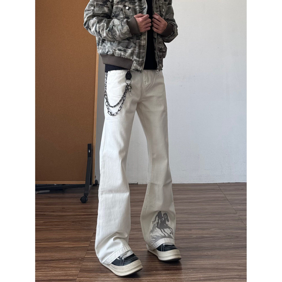 White bootcut jeans with horse graphic embroidery at the ankle and chain belt accessory