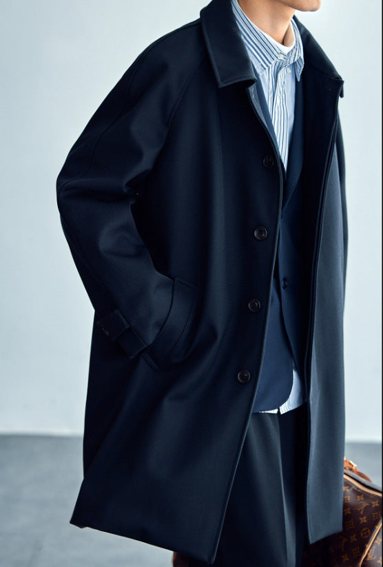 Black wool trench coat with raglan sleeves and button placket, worn open at front.