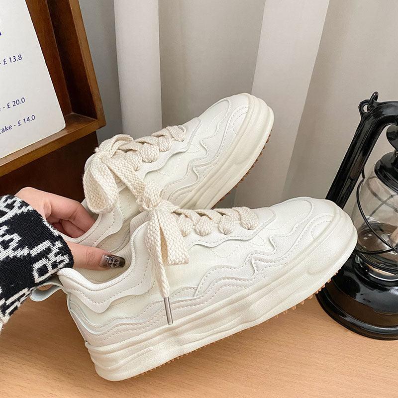 Cream platform sneakers held together by hands, showing lace-up design