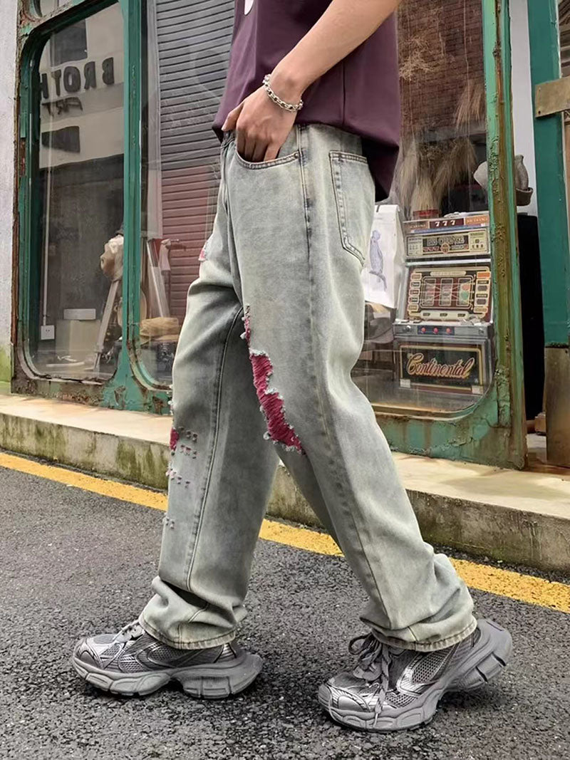 Light wash denim slim-straight pants with red/pink distressed patches, cuffed hems
