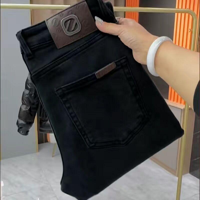 Men's black slim-fit jeans with leather brand waistband patch held up for view