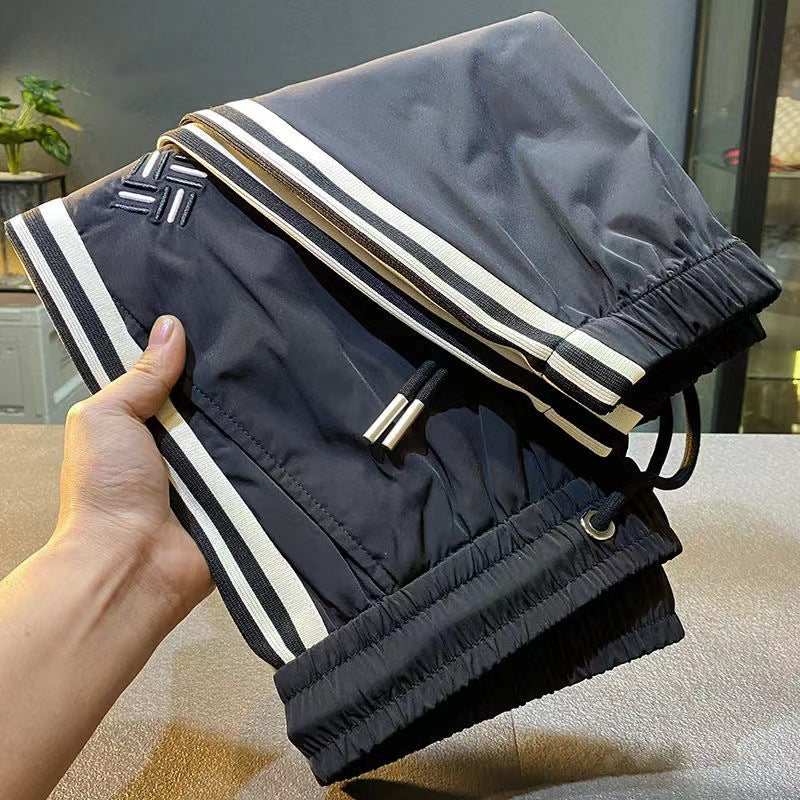 Ice-silk pants in dark navy with white-and-gold side stripes, elastic cuffs, zip pocket detail