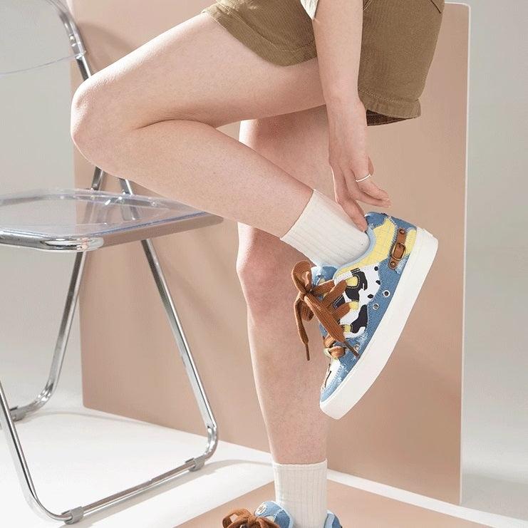 Low-top canvas sneakers with blue cow-pattern patchwork and brown lace-ups.