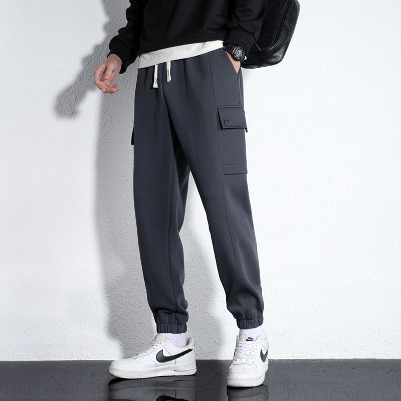 Dark gray cotton jogger trousers with drawstring waist, elastic cuffs, and side flap pocket