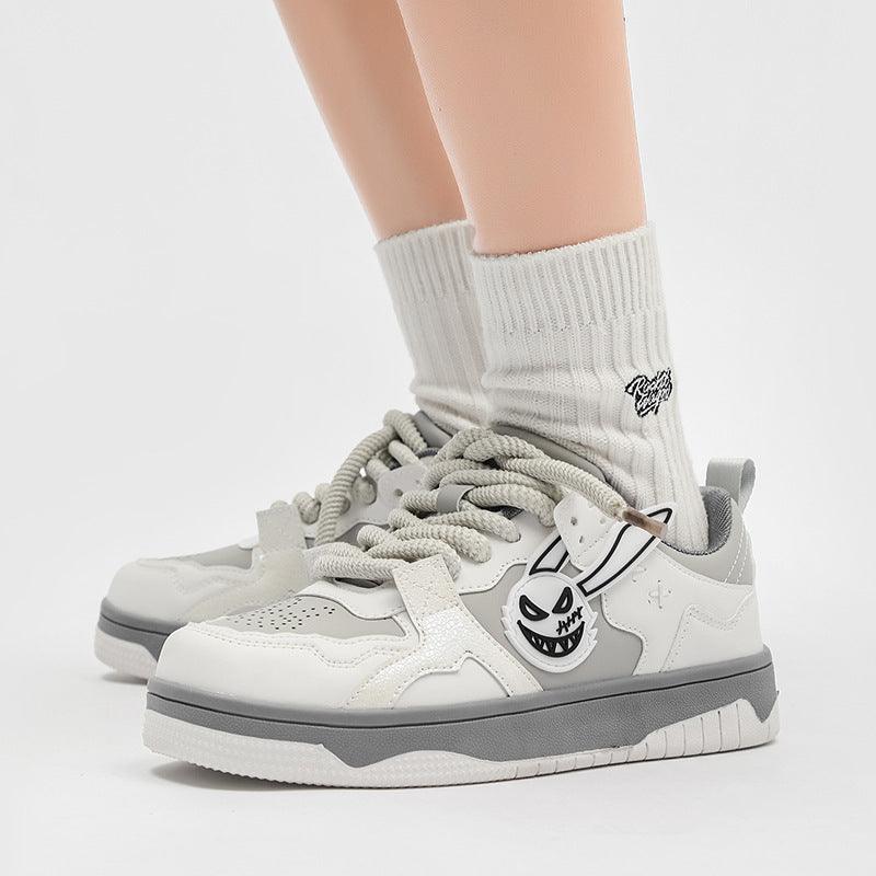 White and gray low-top sneakers with lace-up front and cartoon face logo