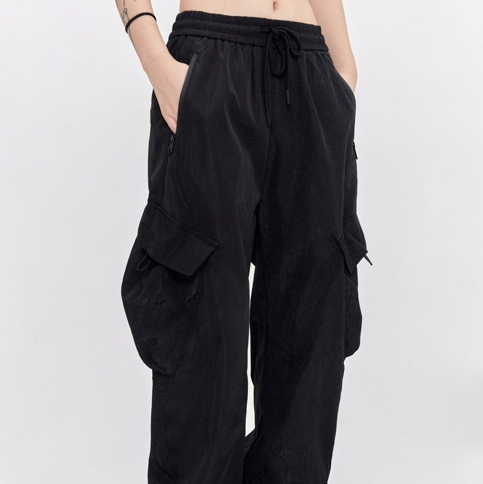 Black pleated cargo trousers with elastic waistband and drawstring, side flap pockets