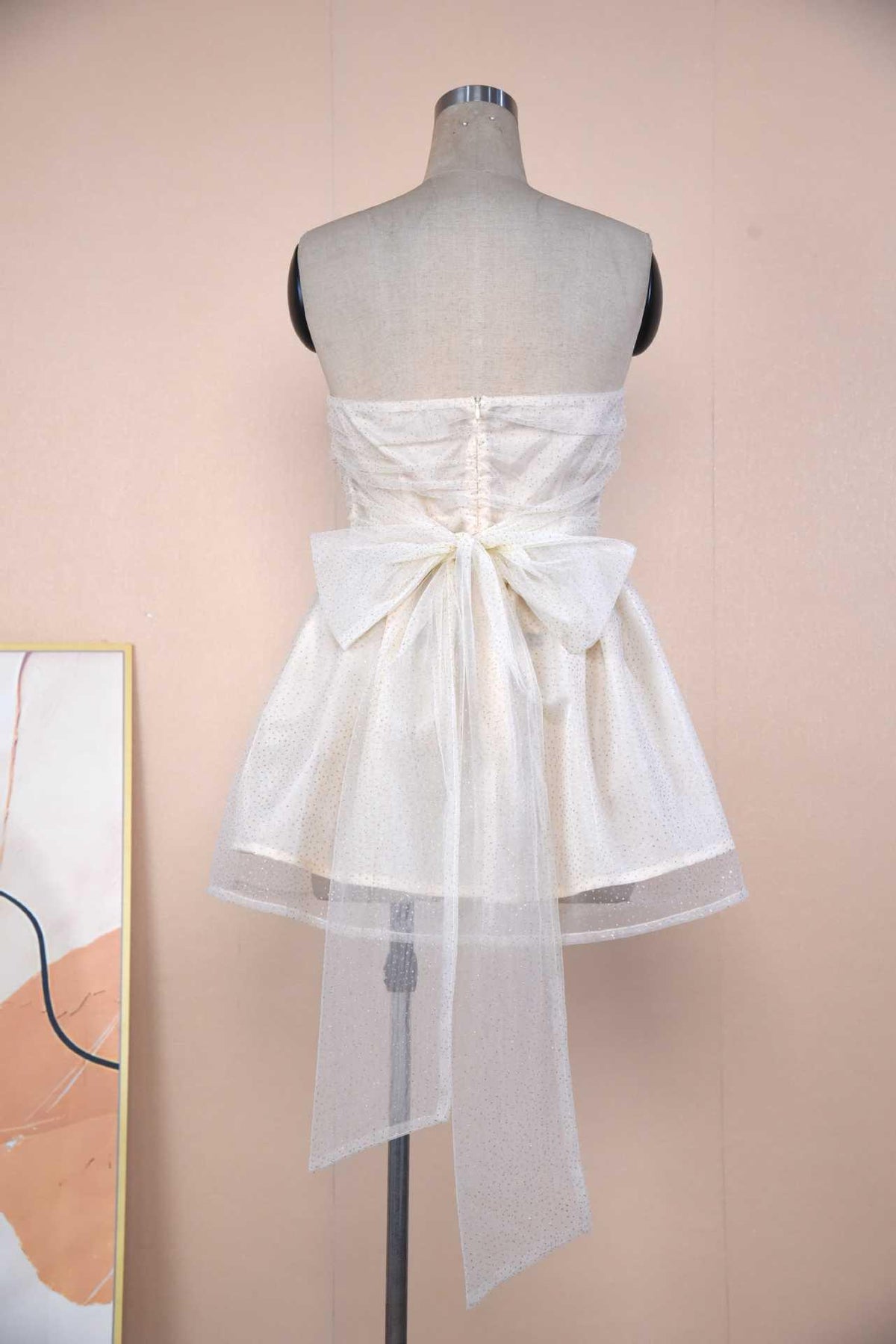 White strapless mini dress on mannequin with ruched bodice and large back bow-knot