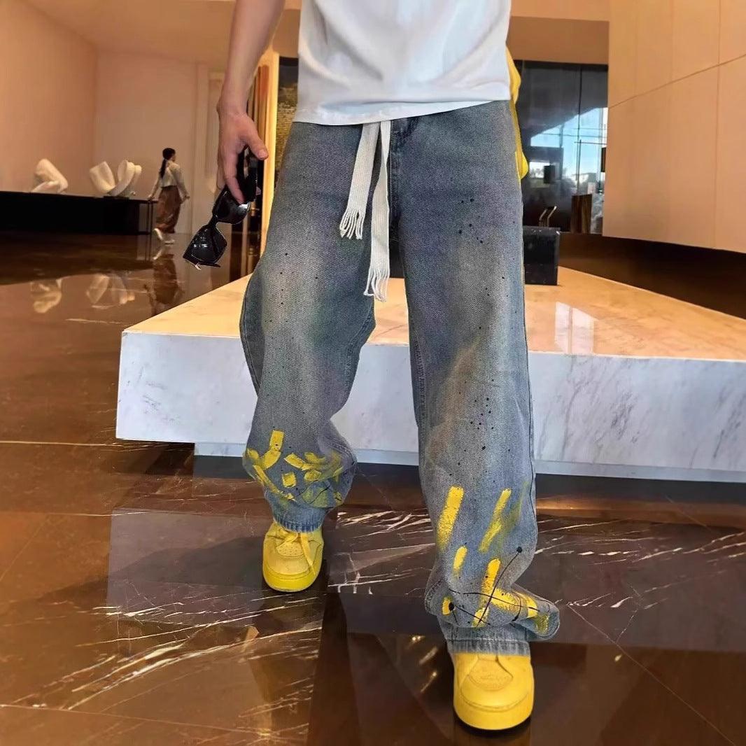 Men's casual light-wash jeans with yellow ink splatter and drawstring ties at waist