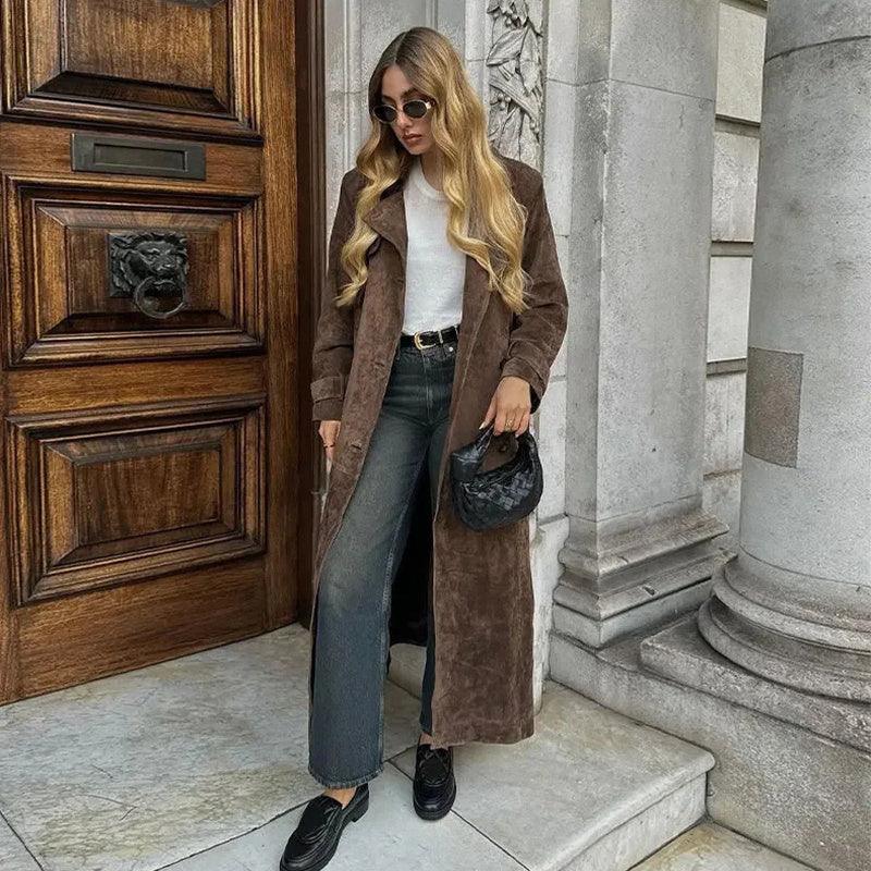 Brown double-breasted long coat with lapels and matching belt, worn open over jeans