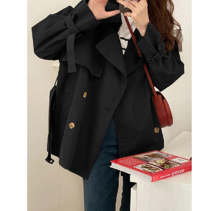 Women’s short trench coat in black, double-breasted front with gold buttons and belt.