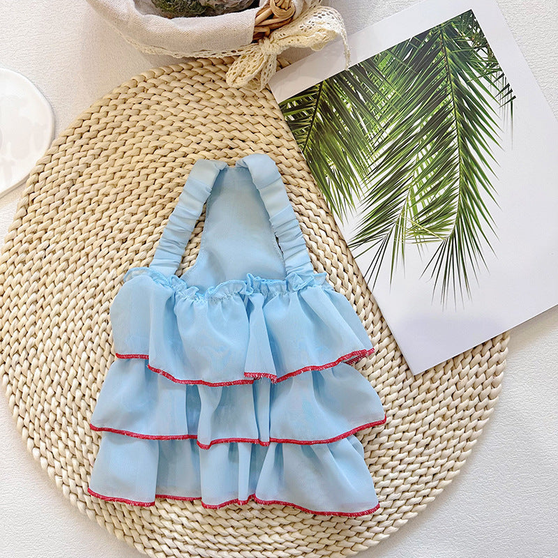 Light blue dog suspender dress with layered ruffles and red trim on straw mat