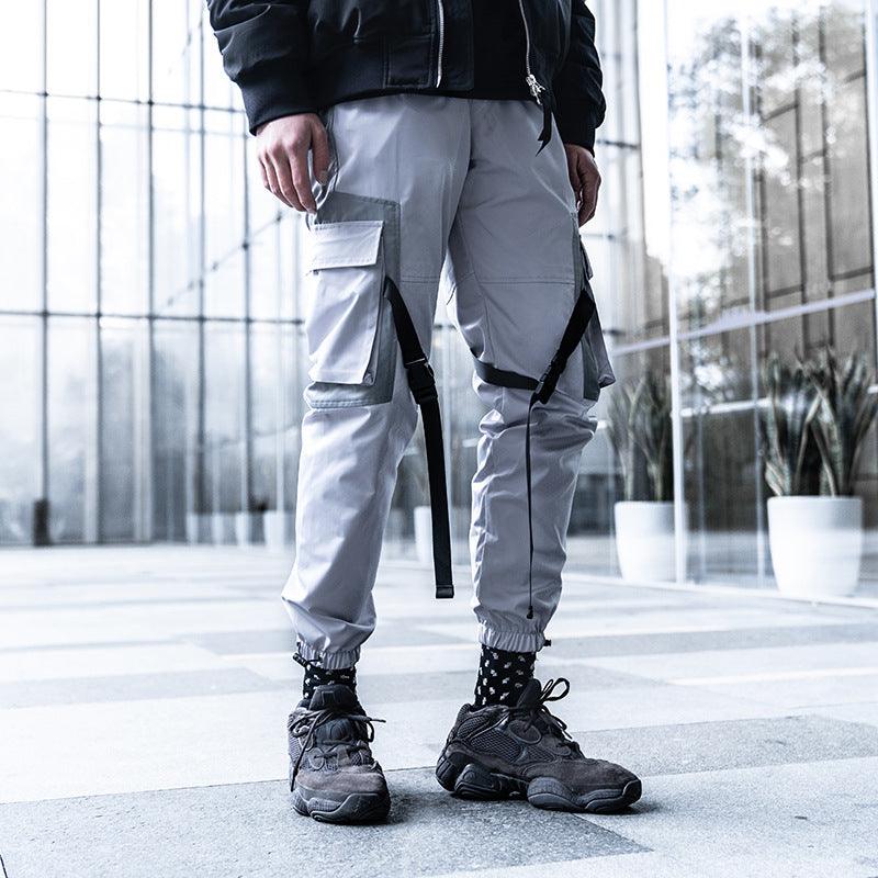 Men's light grey cargo-style trousers with side flap pockets and hanging strap details