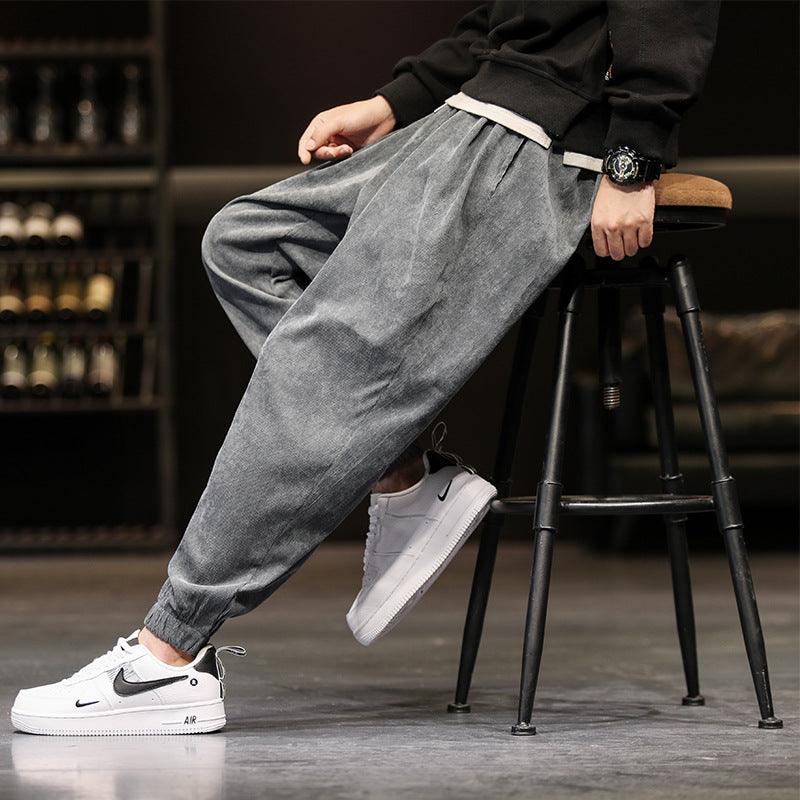 Grey corduroy jogger-style trousers with elastic cuffs and side drape folds
