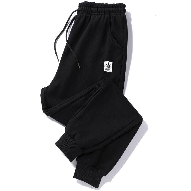 Black jogger trousers with drawstring waist, elastic cuffs, side pocket, and white logo patch