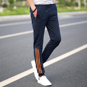 Men's dark blue track pants with orange side stripes and tapered cuffs