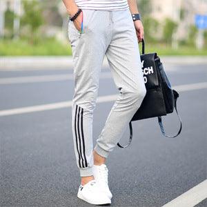 Men's light grey track pants with white side stripes and tapered cuffs