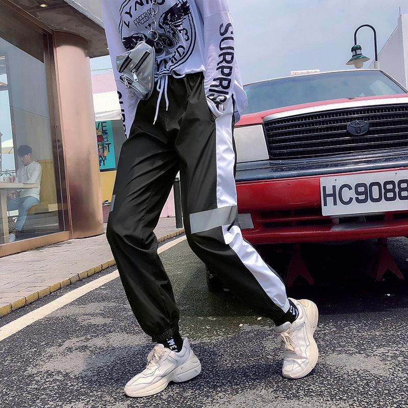 Black track trousers with white side panels and gray reflective stripe near thigh