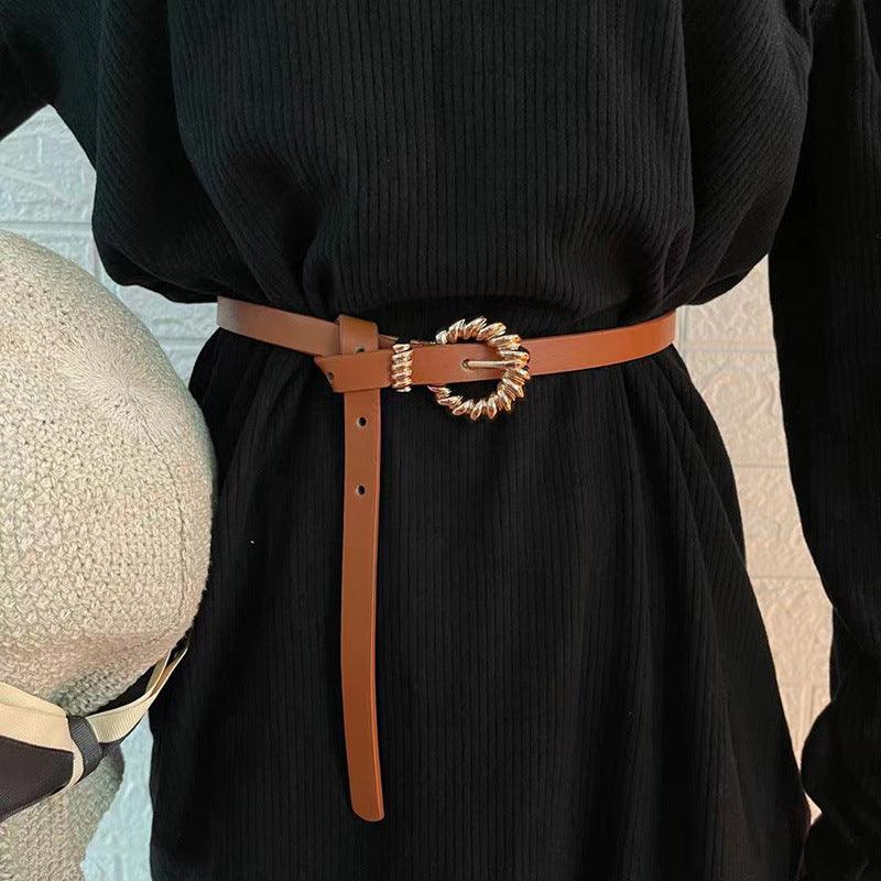 Black thin woven belt with gold-toned ornate buckle and long rectangular end strap