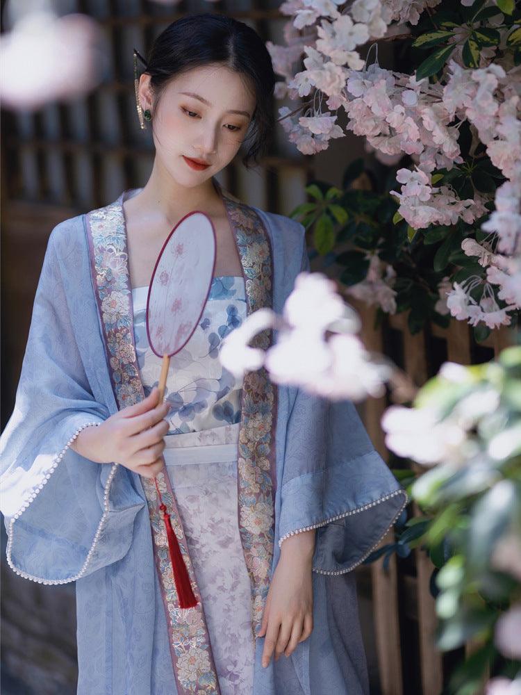 Light-blue floral strapless long dress with sheer outer layer, holding a round fan