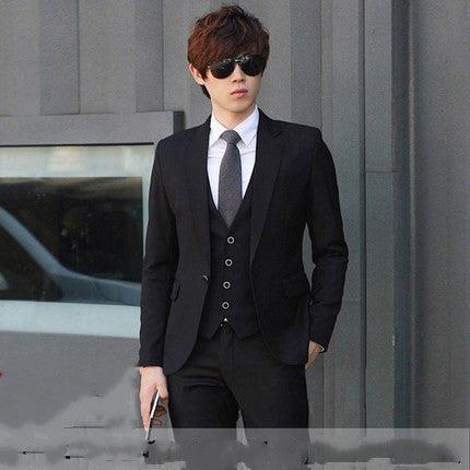 Slim-fit men’s suit in black with matching vest and white shirt, dark tie.