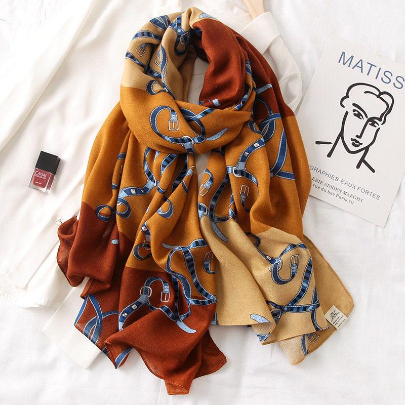 Orange silk scarf with blue strap-like horse patterns, draped with tags.