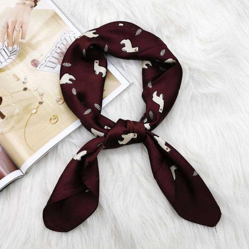 Square satin scarf in dark maroon with white animal silhouettes, tied in a bow