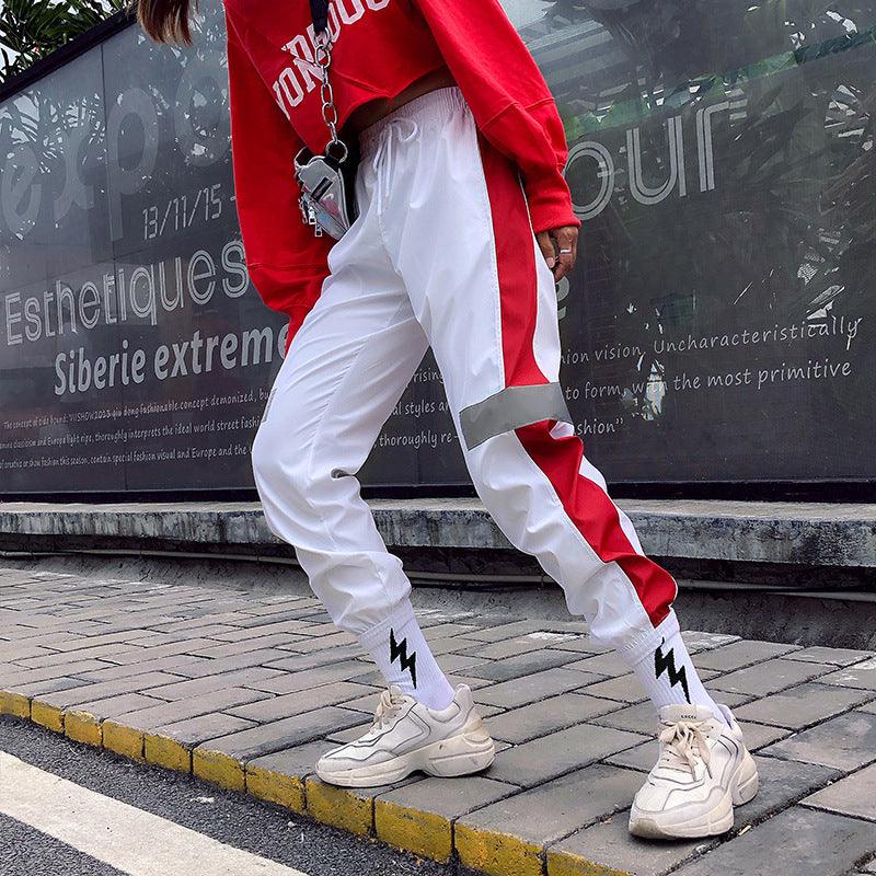 Light-colored track trousers with red reflective side stripe and tapered cuffs