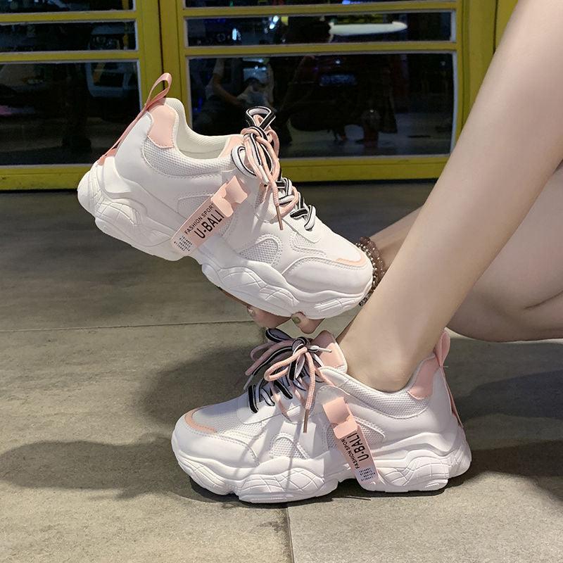 White casual sport shoes with pink laces and trim, chunky sole, tag on tongue