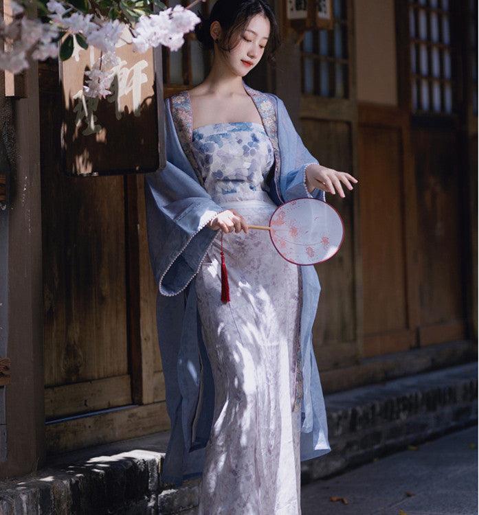 Light-blue floral strapless long dress with sheer outer drape, holding a round fan