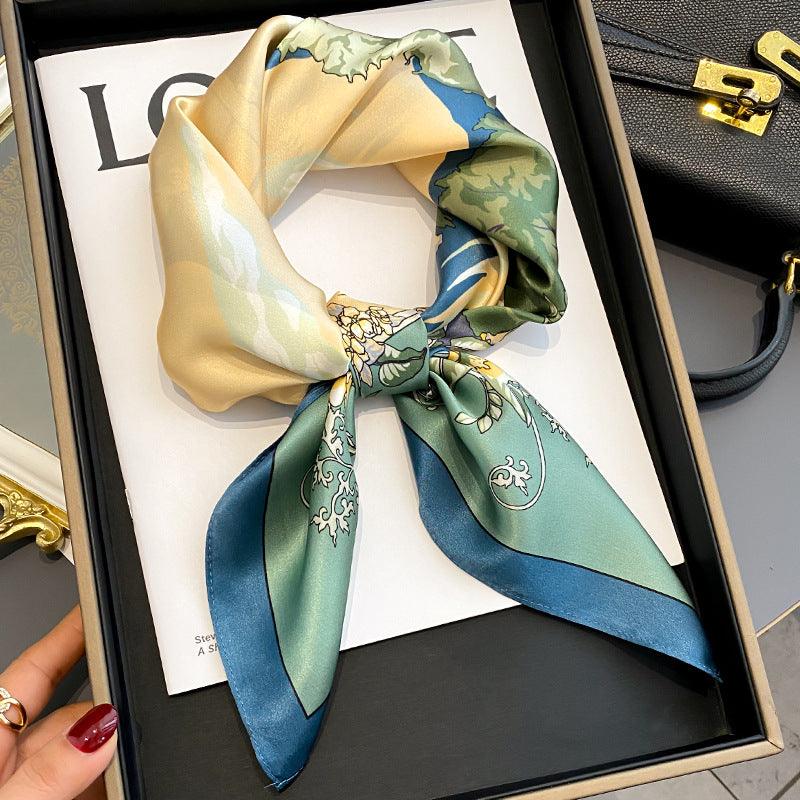 Beige and teal silk scarf with floral vines and blue ribbon-like stripes.